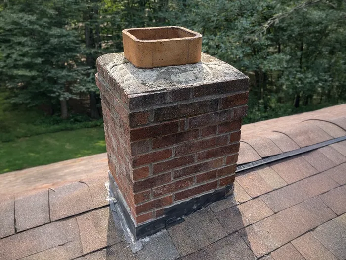 Weathered brick chimney with a cracked crown and exposed clay flue before repair